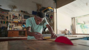 Marangozluk atölyesinde çalışan konsantre olmuş siyah Brezilyalı genç bir marangoz. Tahta kesmeye hazırlanan ahşabı ölçmekle meşgul biri.