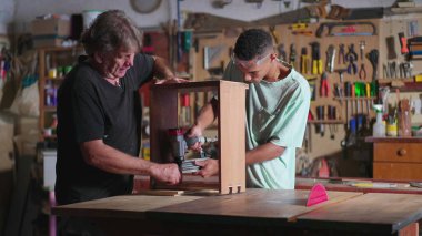 Marangoz atölyesinde çalışan kıdemli marangoz ve genç çırak.