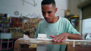 Marangozluk atölyesinde ahşap yüzeyi aletle cilalayan genç bir Brezilyalı marangoz. Çalışanların mesleği mobilya tamir etmektir.