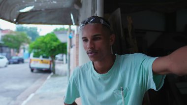 Düşünceli genç bir zenci işçi yerel bir dükkanda dikilip caddeye bakıyor, atölyedeki marangozluğa ara veriyor.