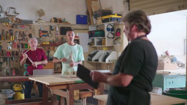 Küçük işletme sahibi, marangozluk atölyesinde elinde tablet bulunan çalışanların online siparişlerini kontrol ediyor. Marangozluk mesleğinde çalışan personel