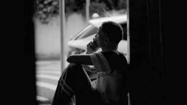 Afro-amerikan kökenli düşünceli biri. Kapıdan komşuları gözlemliyor. Düşünceli bir ifadeyle, dramatik siyah-beyaz.