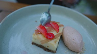 Lüks bir restoranda rafine edilmiş tatlı tabağı, üzerinde çilek dilimleri ve yanında dondurmayla cheesecake tatlısı yemek.