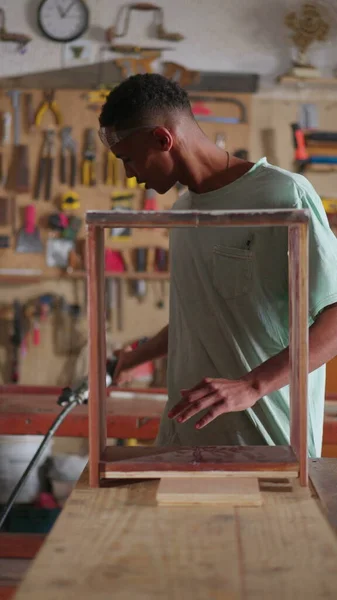 在木工车间工作的年轻木匠学徒 在垂直录像导师的指导下 用钻具修理家具木料 — 图库照片