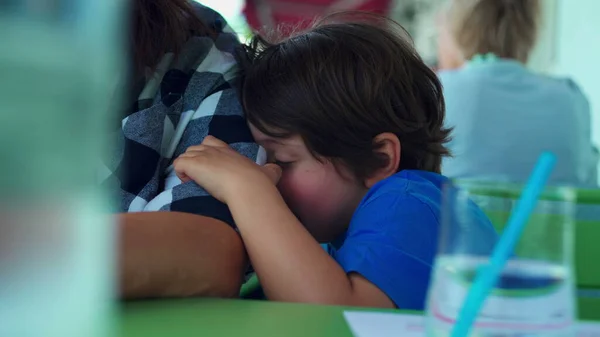 stock image Bored small boy leaning on mother arm feeling boredom at restaurant waiting for food to arrive. Child glued to parent and rubbing face