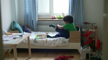 Yatak odasındaki yatağa çorap koymaya çalışan samimi küçük çocuk. Giysilerini giyerken çocuk şikayeti duygularını altüst ediyor.