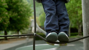 Çocuk oyun sahasında oynuyor halatın üzerinde duruyor ve sonbahar sezonu boyunca metal parmaklıklara tutunuyor, ceketini giyiyor.