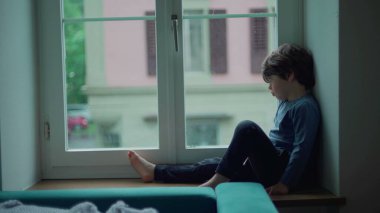 Sıkıcı çocuk yağmurlu bir öğleden sonra pencerenin kenarında oturmuş çiseleyen yağmuru seyrediyor. Küçük çocuk evde takılıp kalmış, dışarı çıkmak istiyor, üzgün düşünceli bir ifade.