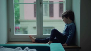 Sıkıcı çocuk yağmurlu bir öğleden sonra pencerenin kenarında oturmuş çiseleyen yağmuru seyrediyor. Küçük çocuk evde takılıp kalmış, dışarı çıkmak istiyor, üzgün düşünceli bir ifade.