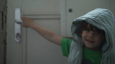 Kapı tokmağını tutan mutlu çocuk, kapüşonlu çocuk girişi açıyor ve dışarı çıkıyor.