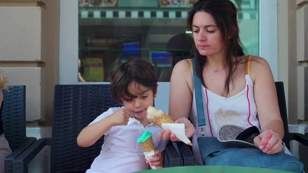 Mother sharing ice-cream cone to son for him to try a different taste. Parent and child enjoying sweet treat, savoring summer food dessert