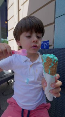Küçük çocuk güneşli bir günde canlı dondurmalı waffle külahının tadını çıkarıyor.