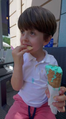 Küçük çocuk güneşli bir günde canlı dondurmalı waffle külahının tadını çıkarıyor.