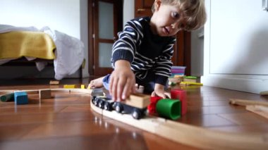 Eski ahşap tren raylarıyla oynayan küçük bir çocuk, hayal gücüne dalmış bir çocuk, eski vagonları elle itiyor.