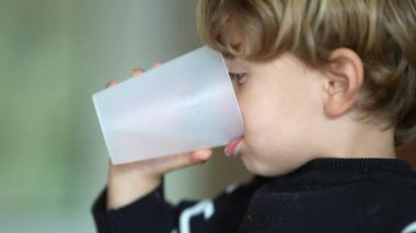Plastik bardakla su içen küçük bir çocuk, beyaz bir erkek çocuğun, suyunu yudumlayan, su içen ve sağlıklı yaşam tarzı kavramının profil yakından görüntüsü.