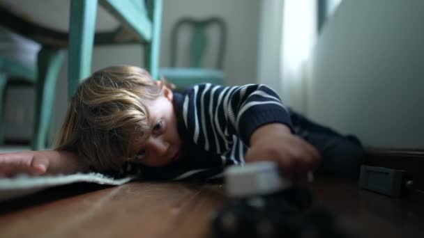 子供は自宅で床で遊んで 1人の小さな男の子は ハードウッドの床に置かれた車のおもちゃを手に持っている彼自身の想像上の世界に従事しました — ストック動画