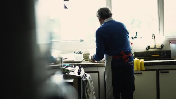 食事を準備するキッチンシンクによるシニアの男の背中 ストーブで自宅で料理するお年寄り — ストック動画