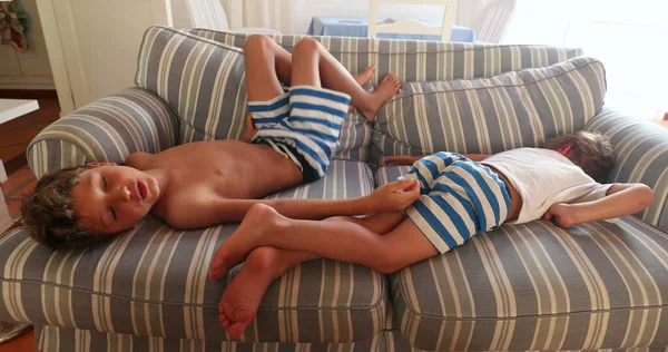 Bored children sitting on sofa. Two kids staying at home with nothing to do