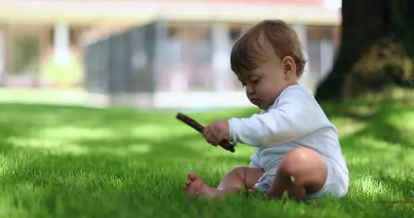 愛らしい赤ちゃんの自宅の芝生の棒を保持する外に座っている かわいいです幼児遊びますとともにスティック屋外 — ストック写真
