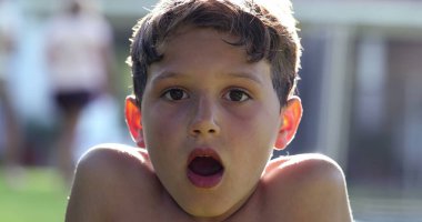 Boy reacting in shock to news with mouth open. Child looking to camera in disbelief and surprise