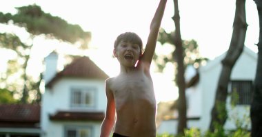 Boy raising arms in the sky clenching fists in victory and celebration with lens-flare sunlight