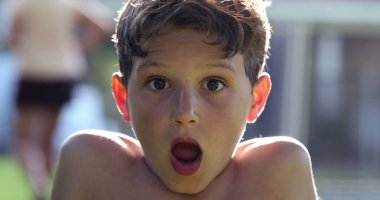 Boy reacting in shock to news with mouth open. Child looking to camera in disbelief and surprise