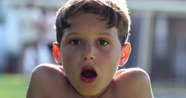 Boy reacting in shock to news with mouth open. Child looking to camera in disbelief and surprise