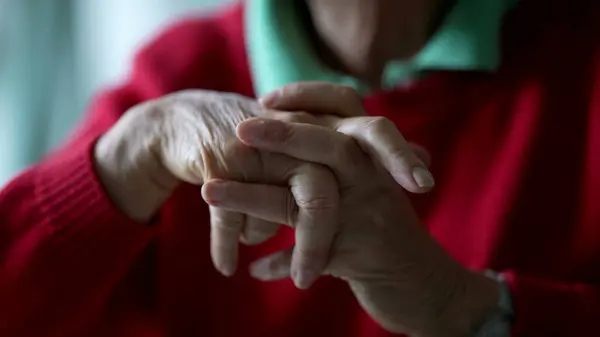 Close-up senior hands clenched in contemplation. Pensive body language of elderly lady in 70s old age, detail hand