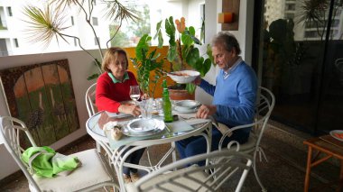 Üst düzey bir çift öğle yemeği için terasta oturuyor. Evli karı koca balkonda yemek, ev hayatı ve emeklilik yılları sunuyor.