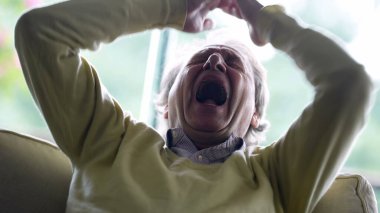 Elleri başının arkasına sıkışmış, esnemekten yorgun düşmüş yaşlı bir adam. Uykulu, sıkılmış, yaşlı, beyaz bir erkek. Yorgunluk ve bıkkınlık hissediyor.