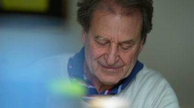 Öğle yemeği saatinde aile üyesiyle kamera dışında etkileşim kuran samimi kıdemli bir adam. 70 'li yaşlarda beyaz, mutlu bir erkek.