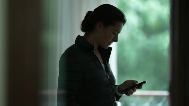 Evdeki cep telefonu cihazına bakan bir kadın, akıllı telefon cihazına bakan samimi bir insan, teknolojiyi kullanarak içeride duran bir ekrana bakıyor.