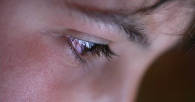 Child eye close-up tablet screen display. Young boy eyes staring at blue light at night
