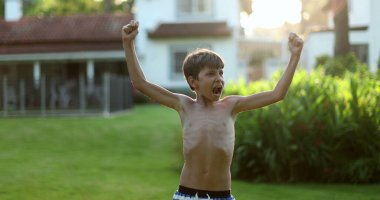 Child raising arms in the air in celebration. Happy victorious young boy raises arm in the air celebrating