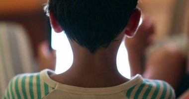 Child staring at tablet device screen at night. Back of boy browsing internet online