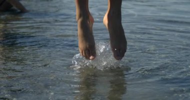 Çocuk bacakları süper yavaş çekimde zıplıyor. Su dalgaları ile 800 fps, küçük bir kız yüksek hız kamerasıyla yukarı zıplıyor, doğayla temas halinde.