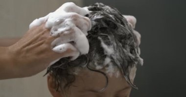 Ebeveynin eli, genç çocuğun saçına köpürüyor, 800 fps yavaş çekim, çocuk aktif olarak hız rampası ile yıkanmaya katılıyor.