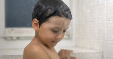Su damlacıklarını izleyen küçük bir çocuk duş banyosunda dururken çok yavaş bir şekilde düşüyor.