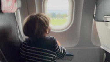 Happy child traveling by plane. Little passenger boy seated inside airplane looking out plane window. Flight departure take off concept.