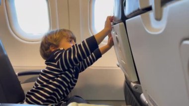  Baby child opening and closing airplane tray table. Little passenger boy seated inside plane cabin. Family lifestyle traveling concept