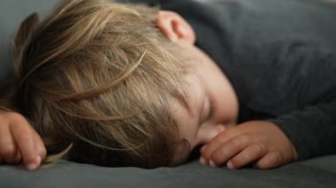  One cute child sleeping. Closeup toddler baby napping. Blond caucasian small boy asleep on couch.