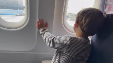 Passenger child looking through plane window. Lifestyle family traveling on vacation concept