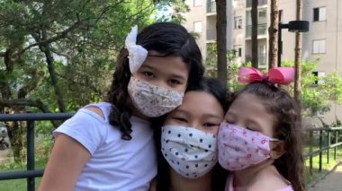 Family wearing face masks outside at park during pandemic epidemic. Three people. Children and mother.