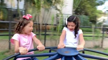 Small girls playing in playground carousel roundabout in motion