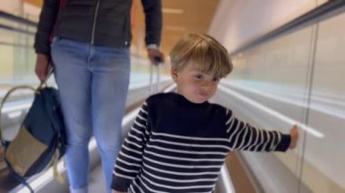  One cute little boy standing at moving corridor at airport. Child traveling. Vacation concept.