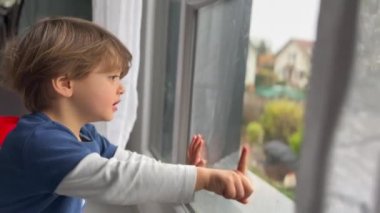 Child stuck at home sitting by window. Little boy wanting to go outside points hand outdoors