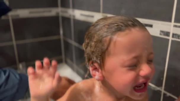 泣いている子供がお風呂に入る 涙を流す小さな少年がシャワーを浴びながら泣いている バスタブでウプセットの子供 — ストック動画