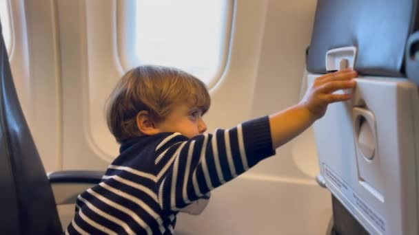 子供を開くトレイテーブルと誤って怪我を取得します 飛行機の中に座っている乗客の少年 — ストック動画