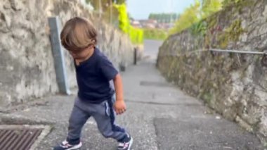 One upset little boy going uphill. Effortful tired child climbing up on road.