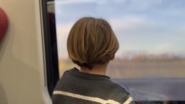 Back of child traveling by train looking at landscape pass by. Kid travels on high speed transportation